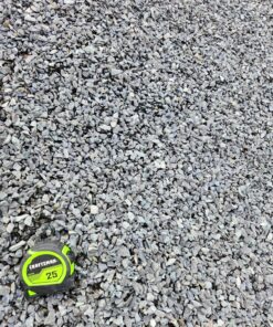An overhead shot of a pile of half-inch gray gravel. A green and black "CRAFTSMAN 25'" tape measure is in the bottom left corner, providing a sense of scale for the size of the rocks. The gravel is light gray and has a rough, angular texture.