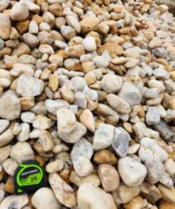 An overhead photo of a pile of large, rounded stones and pebbles. The rocks are a variety of sizes and colors, including shades of white, gray, tan, and brown. A green and black "CRAFTSMAN 25'" tape measure is in the bottom left corner, providing a sense of scale.