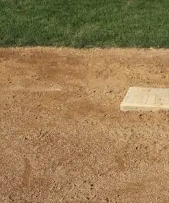 A ground-level photo of a baseball field's second base. The base is a white canvas bag with a dark shadow and is sitting on a patch of light brown, grainy dirt. A line of green grass is visible in the background, separating the infield from the outfield.
